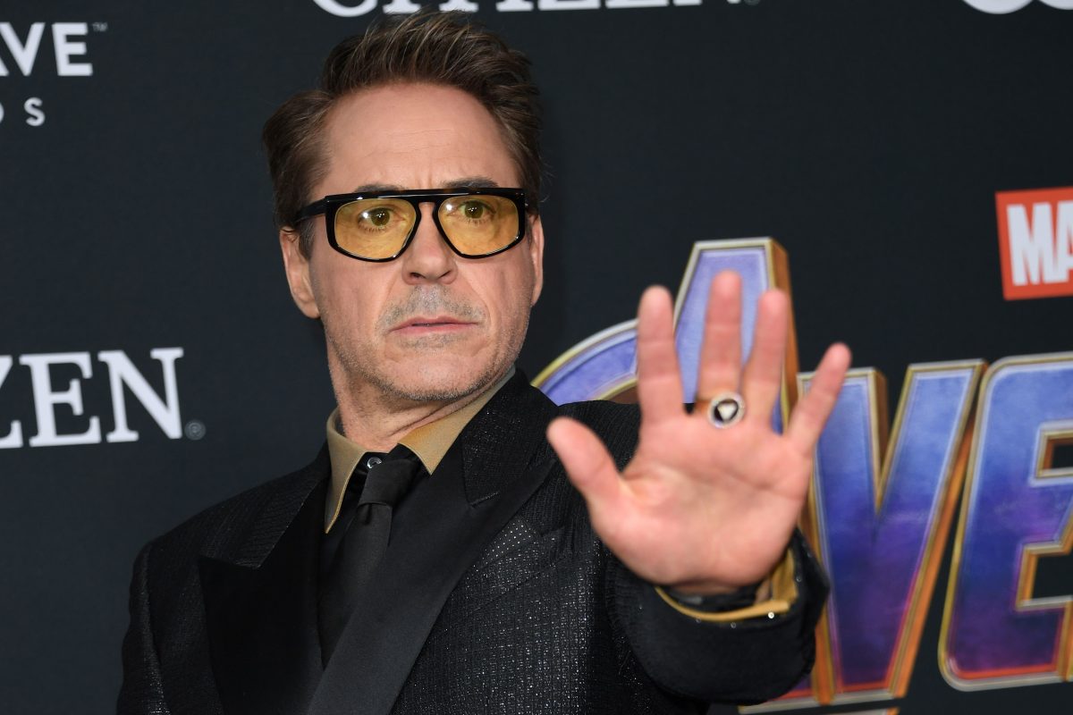 Robert Downey jr. doing an Iron Man pose in a suit and tinted glasses