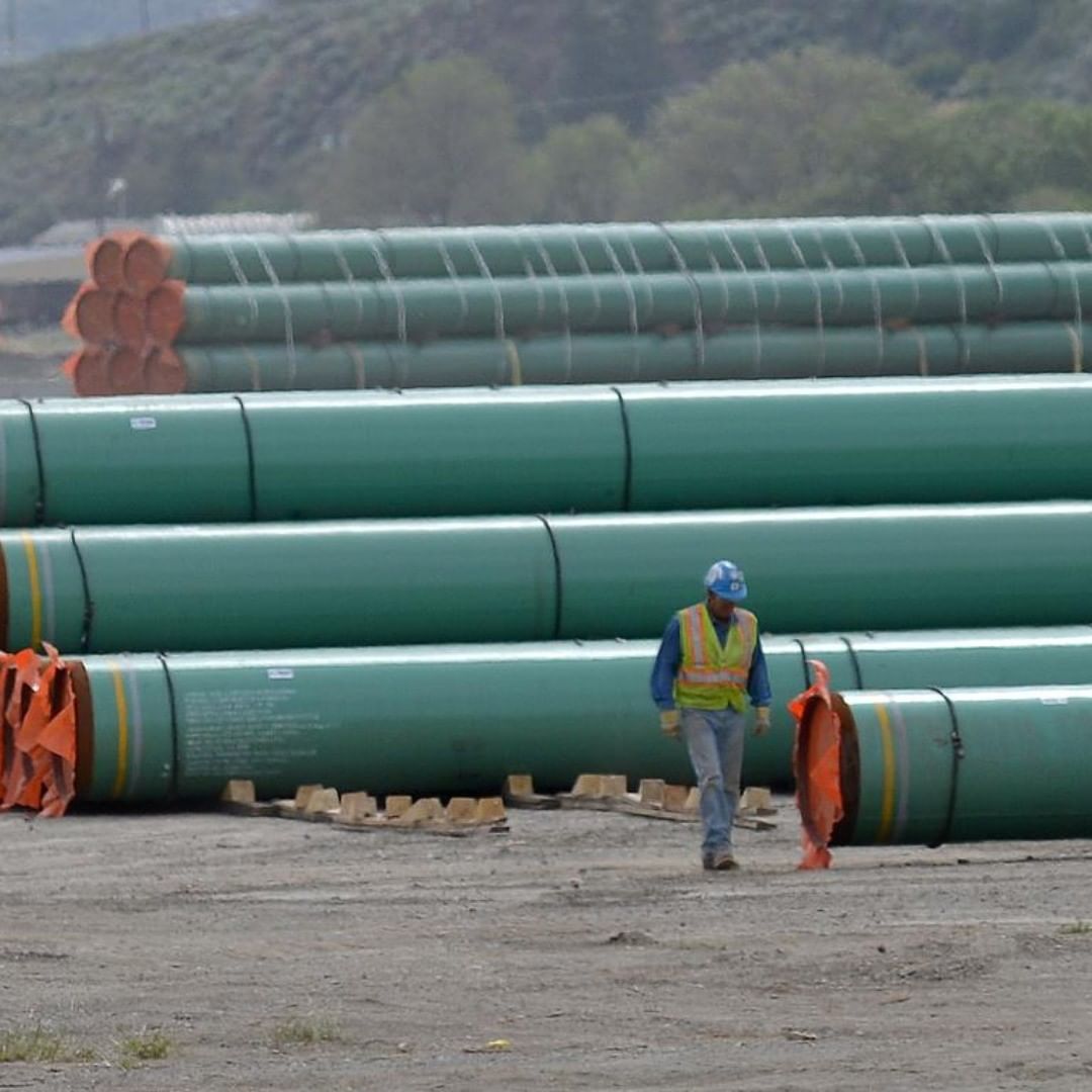 A worker in a hard hat walks past massive oil pipes