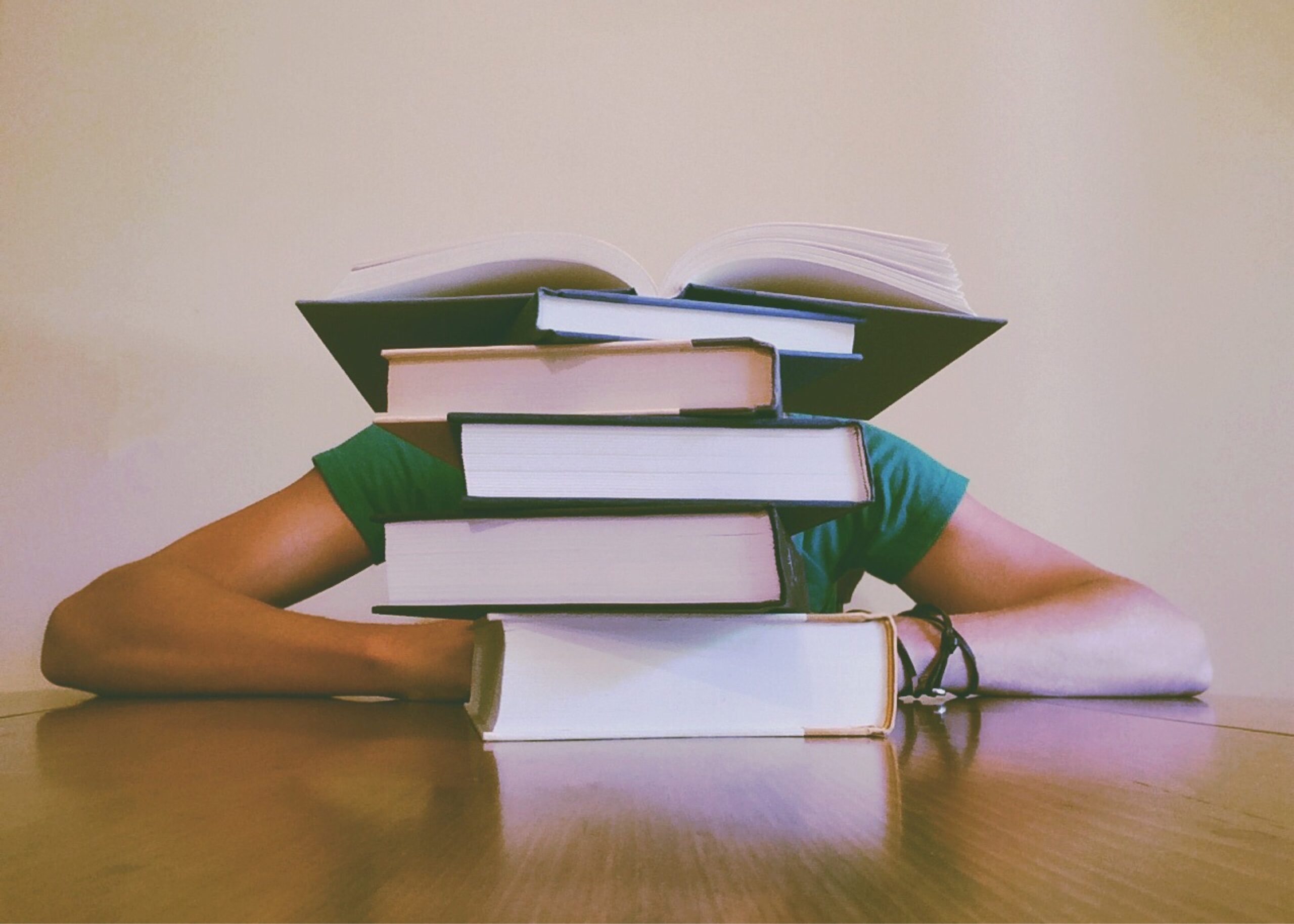 A person in green laying her head on the table with stacks of books in front