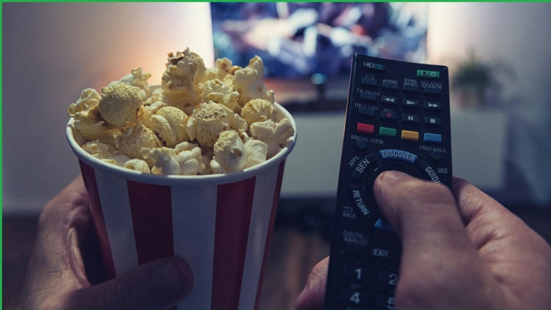 A man holding a remote control and popcorn while watching TV
