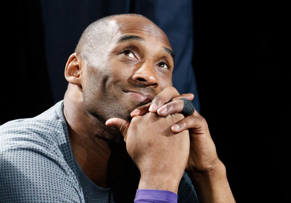 Kobe Bryant wearing a blue dotted shirt and smiling while looking up