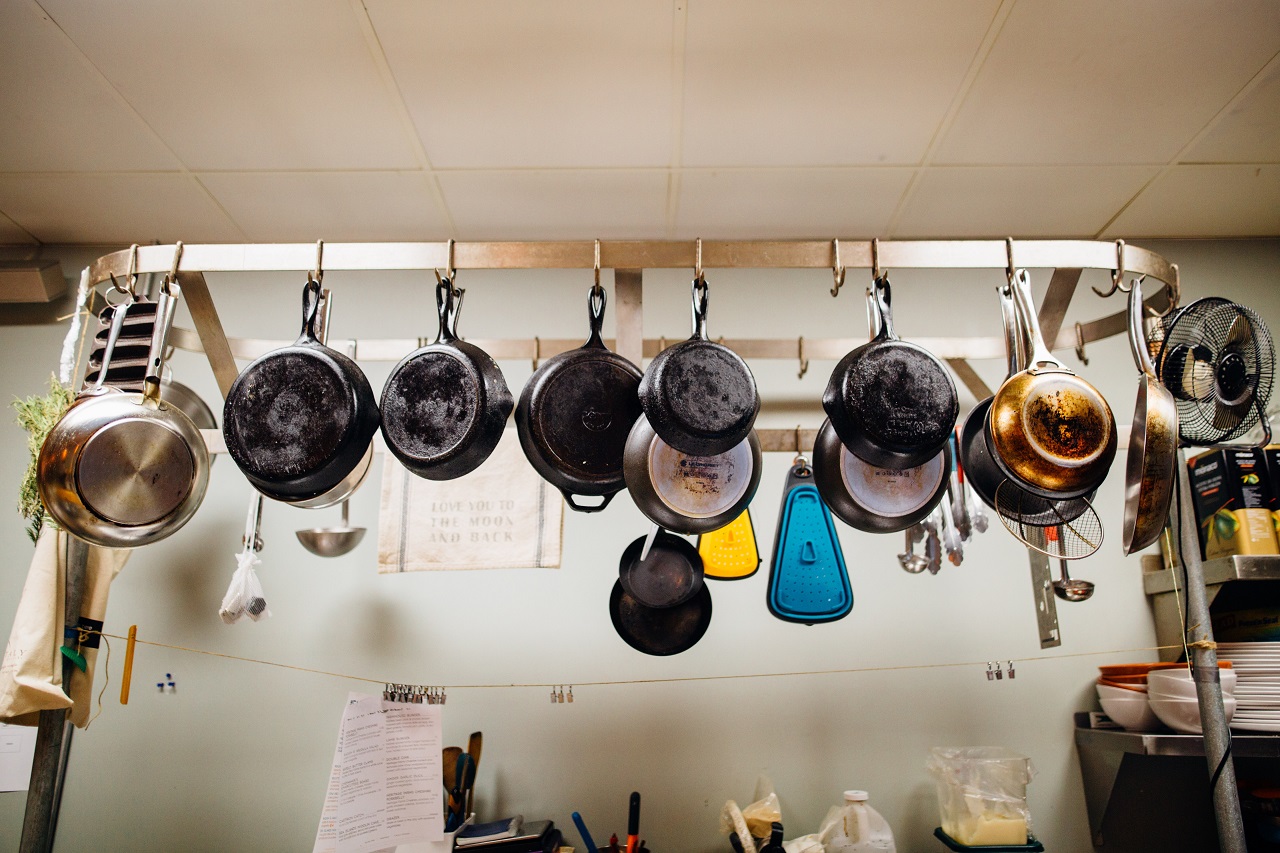 Fifteen different kinds of non-stick pans hanging from a kitchen rack along with ladles and strainers