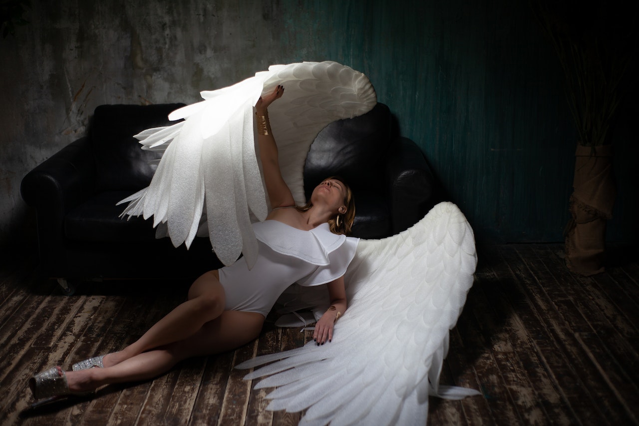 Graceful woman wearing angel wings lying on floor