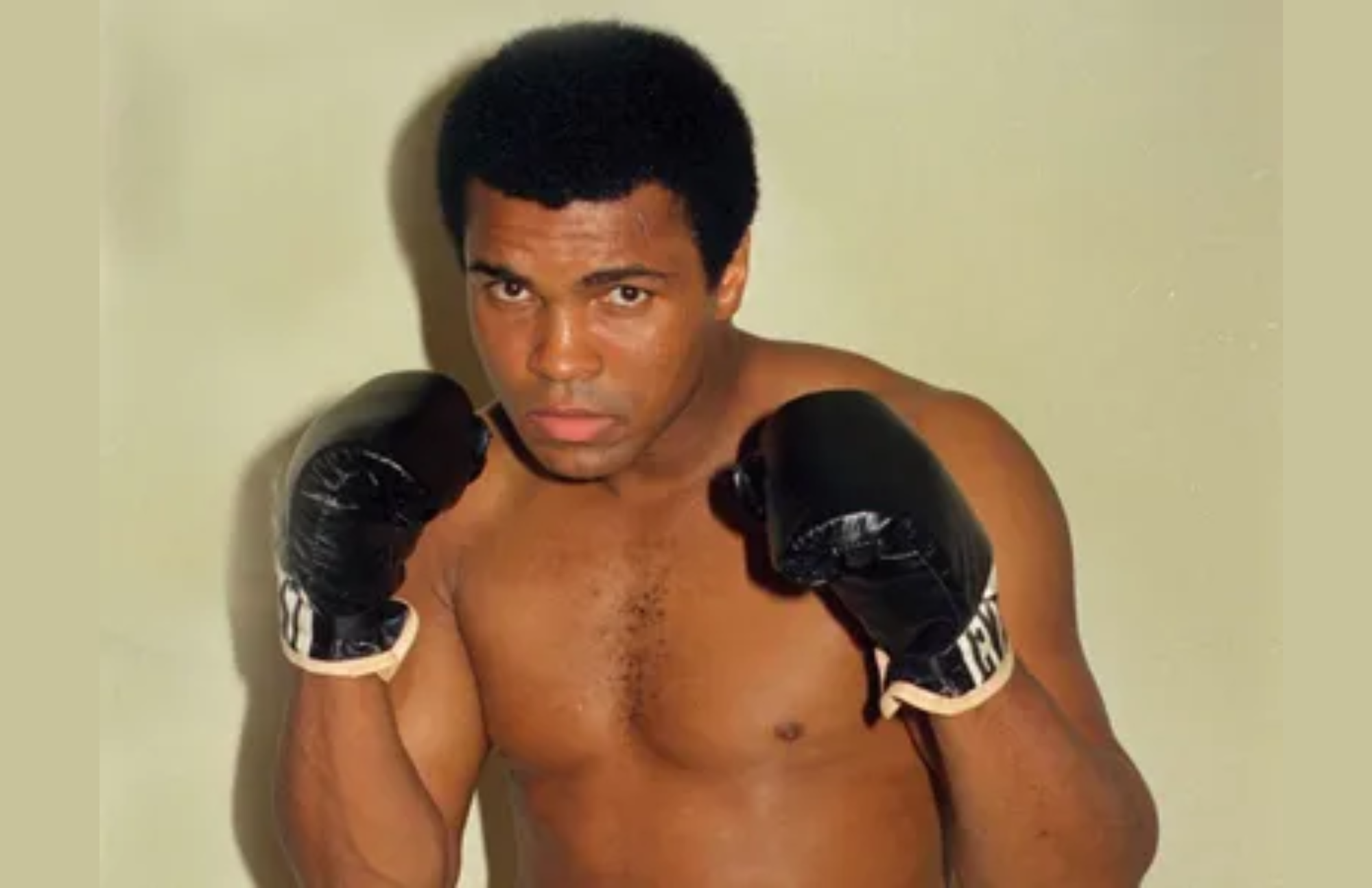 Muhammad Ali poses while wearing his black boxing gloves