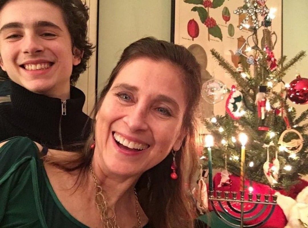 Nicole Flender and Timothee Chalamet smiling beside a small Christmas tree