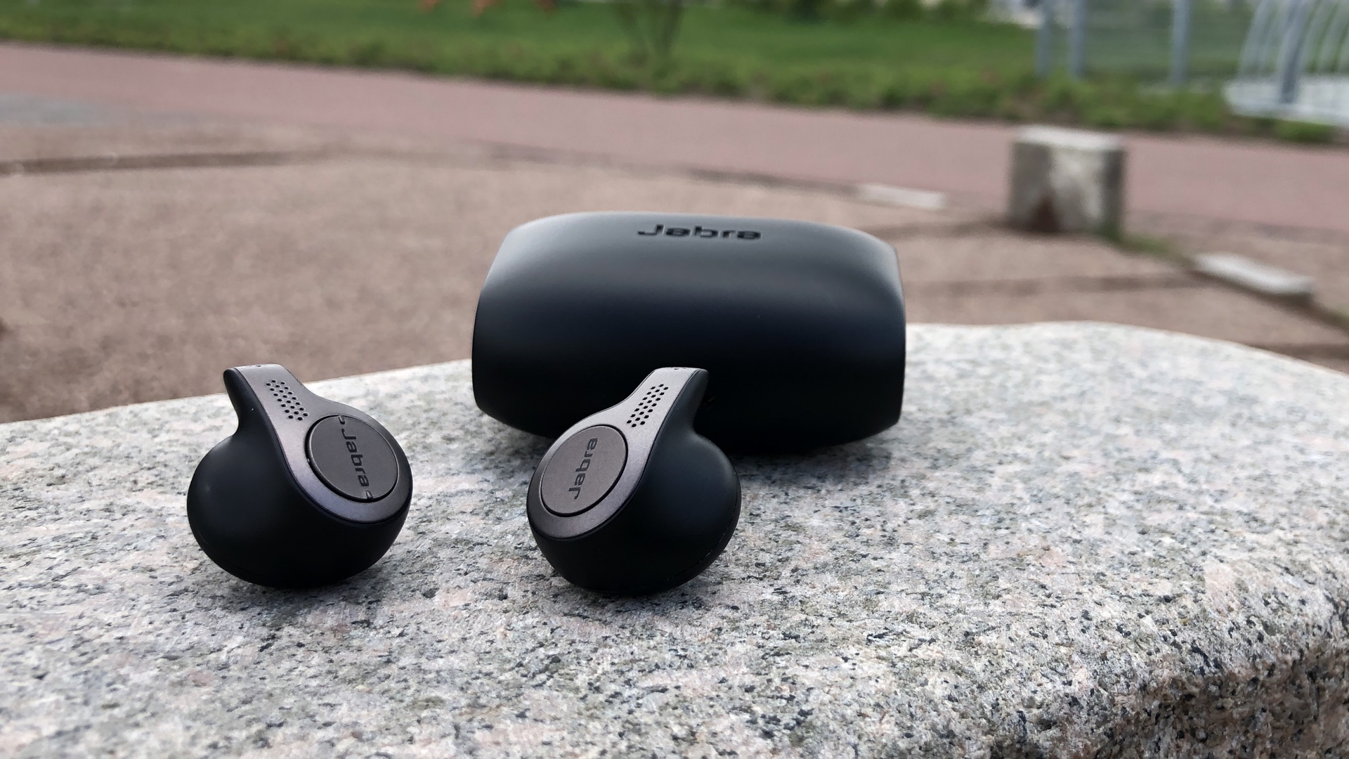 Jabra Elite 65t pair and its case placed on rock in the garden