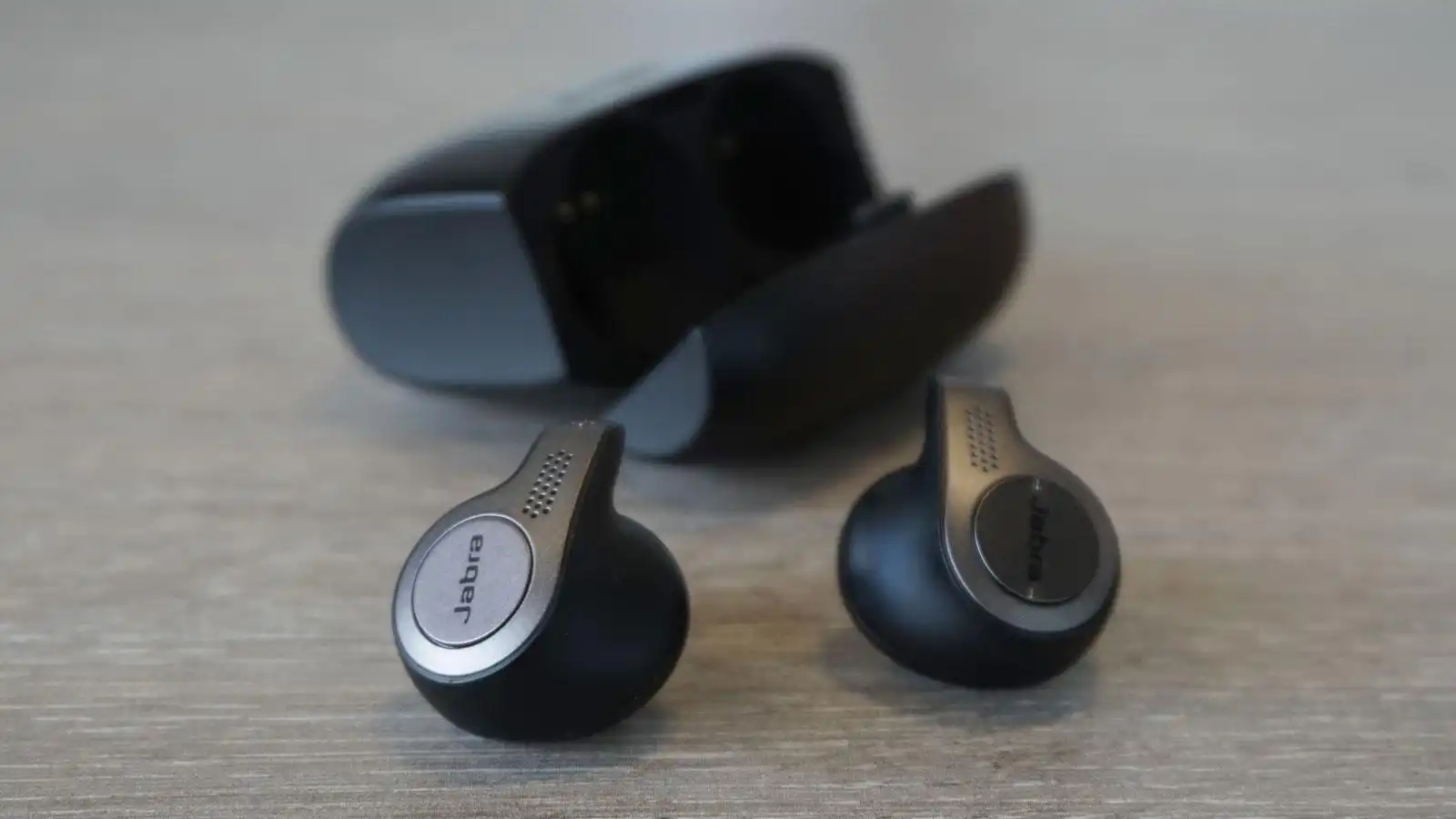 Black and silver Jabra Elite 65t pair and its black case on a table