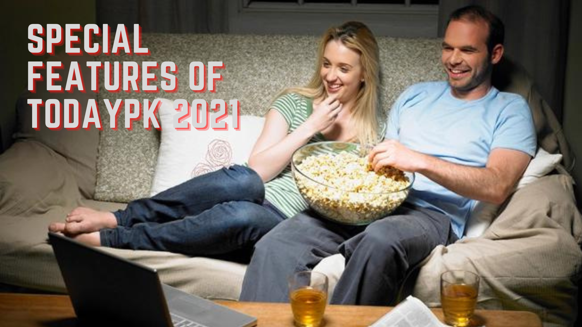 A couple sitting on a couch and watching movie from a laptop while eating popcorn