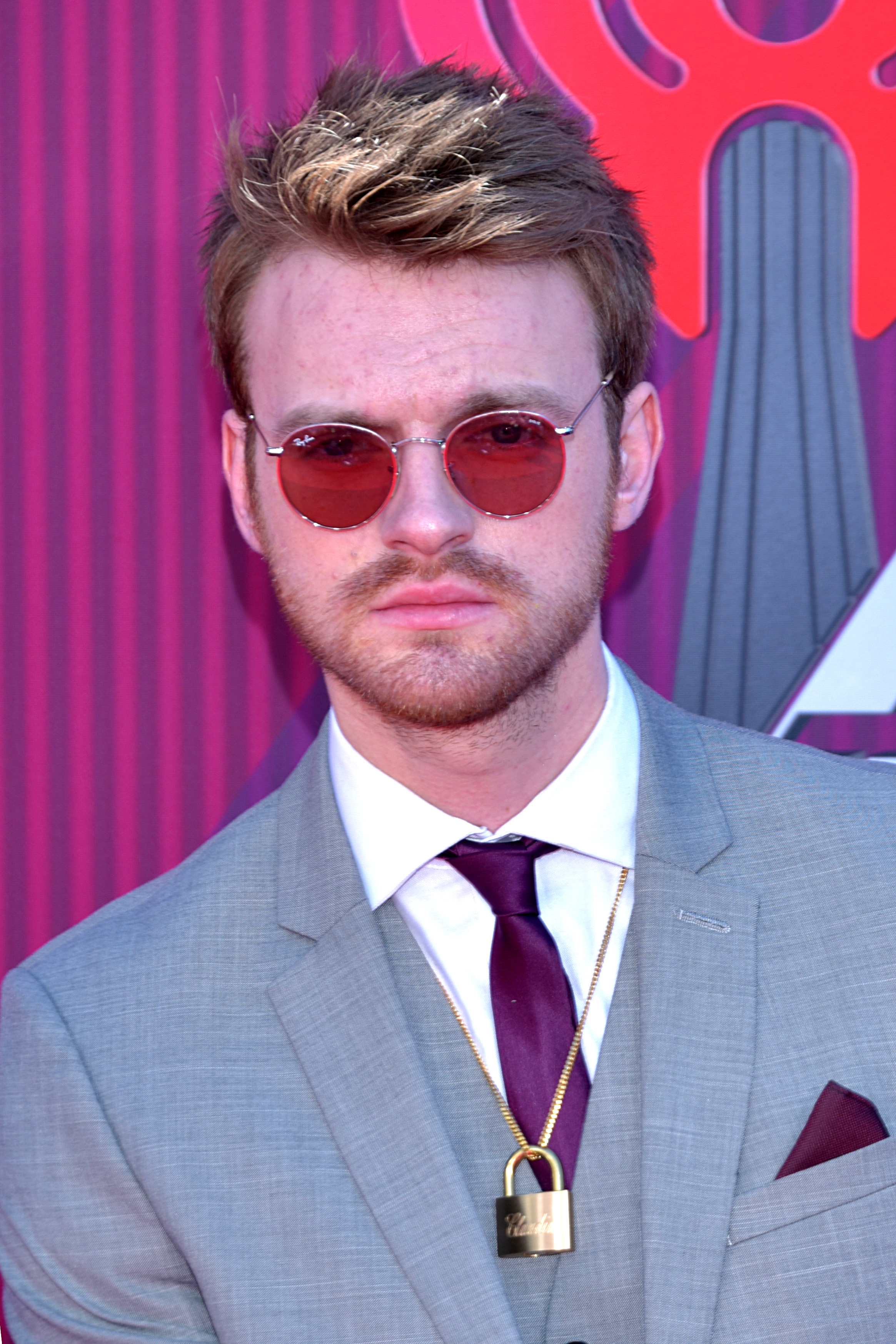 Finneas O'Connell wearing a grey suit and a golden lock neck-piece