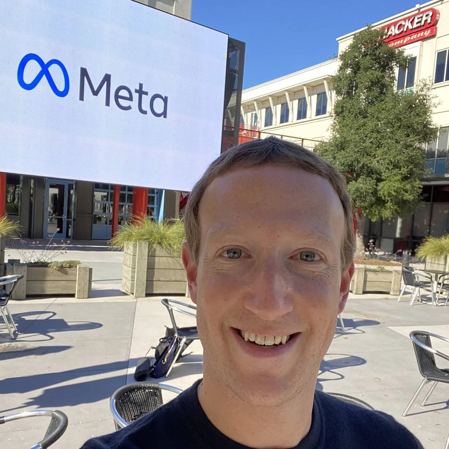 Mark Zuckerberg takes a selfie outdoors, with back from a Meta billboard sign