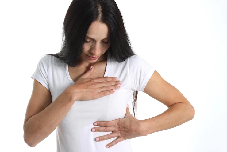 A woman in a white shirt has both hands on her left breast