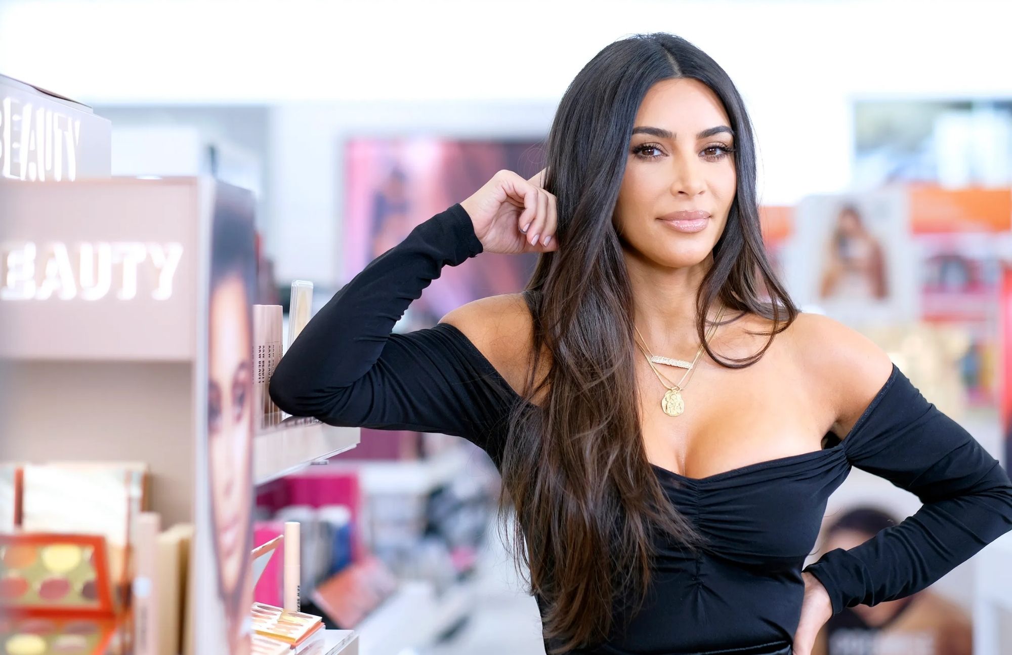 Kim Kardashian is wearing a black dress and leaning against the cosmetic sideboard inside the beauty shop