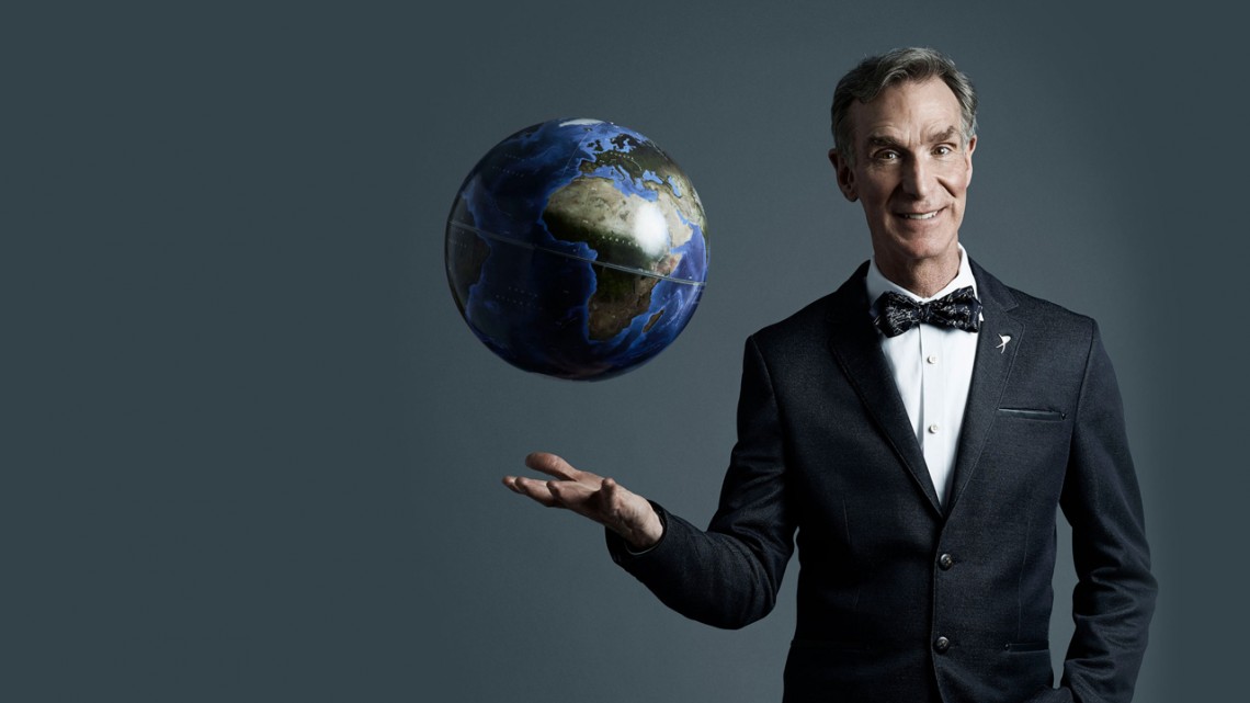 Bill Nye wearing his usual suit and bow tie with a globe floating above his right hand