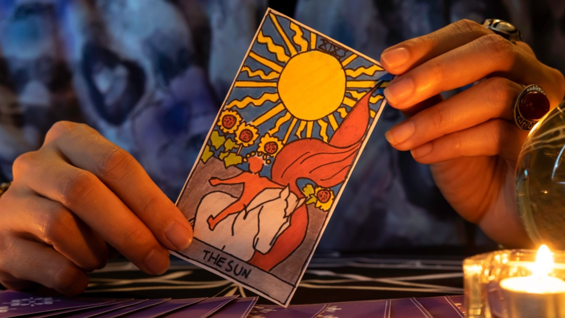 A person holding a sun tarot card with a candle on the right
