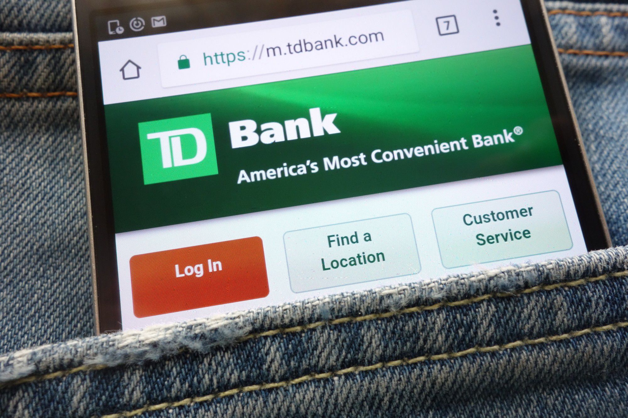 A grey jeans pocket containing mobile phone with TD card services website on its screen