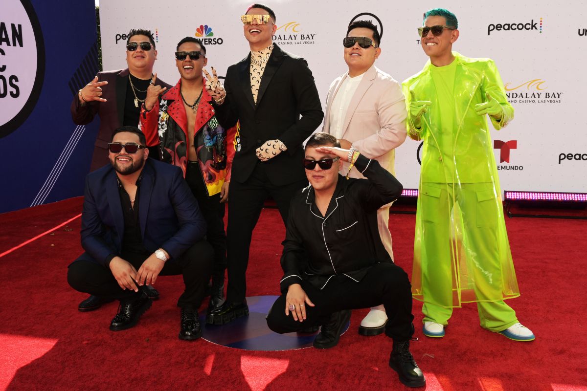 Grupo Firme smiling and wearing colorful outfits and black sunglasses in an event