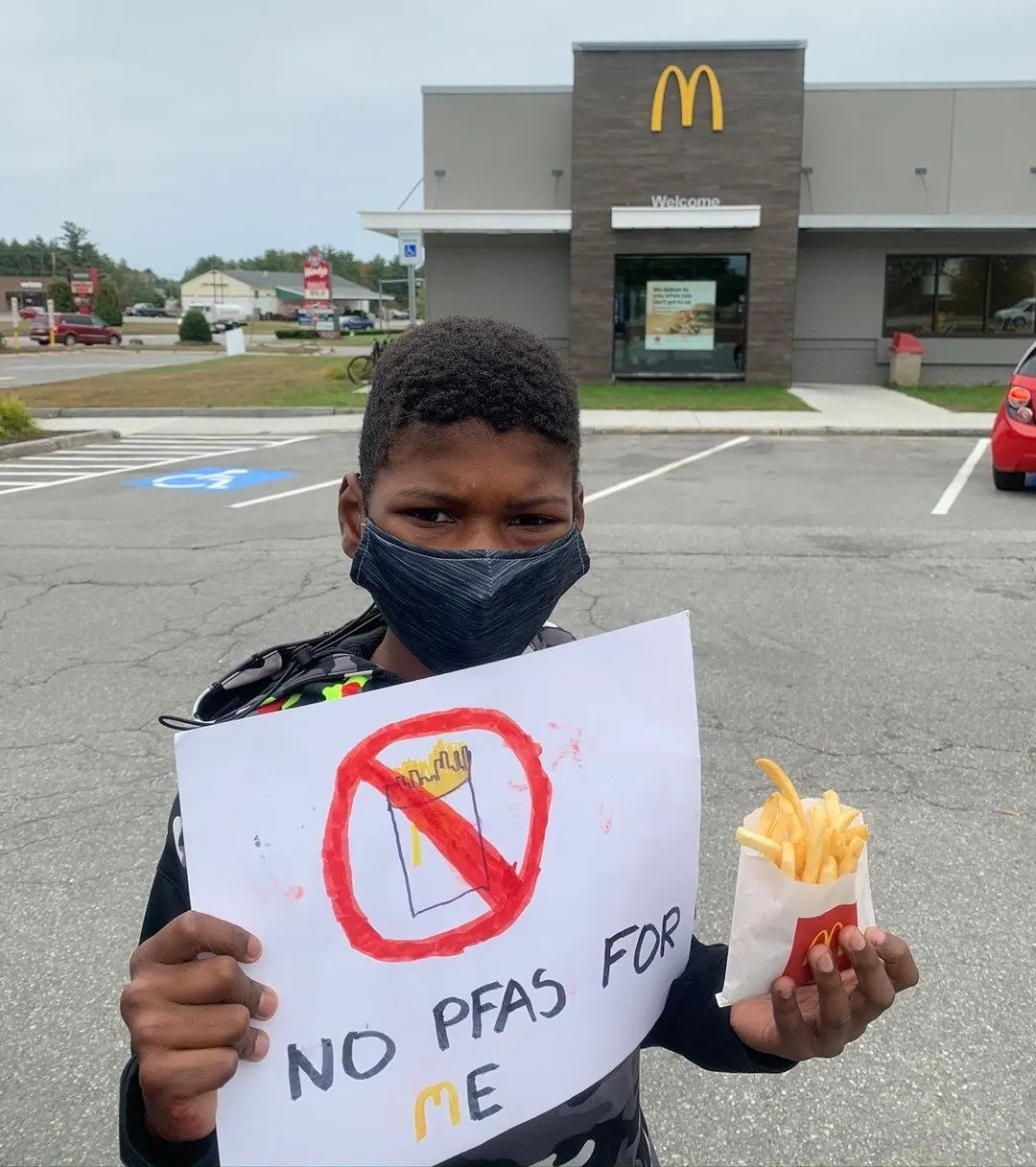 A male kid outside McDonald’s holding McDonald’s fries and a handwritten sign that says, ‘no PFAS for me’