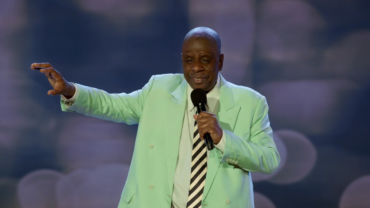 JJ Walker holding a mic and raising his arm while wearing pastel green suit