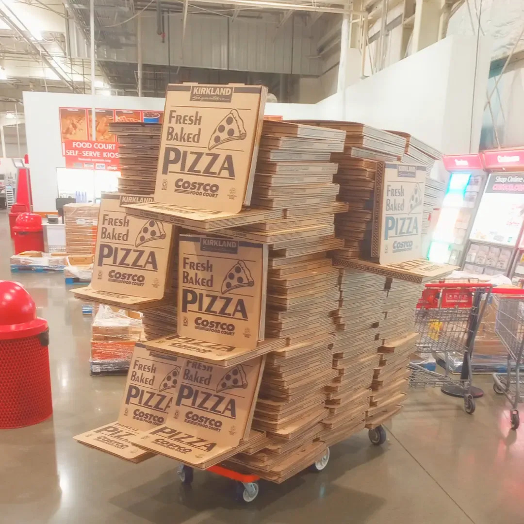 Stacks of brown Costco pizza boxes on a flatbed trolley