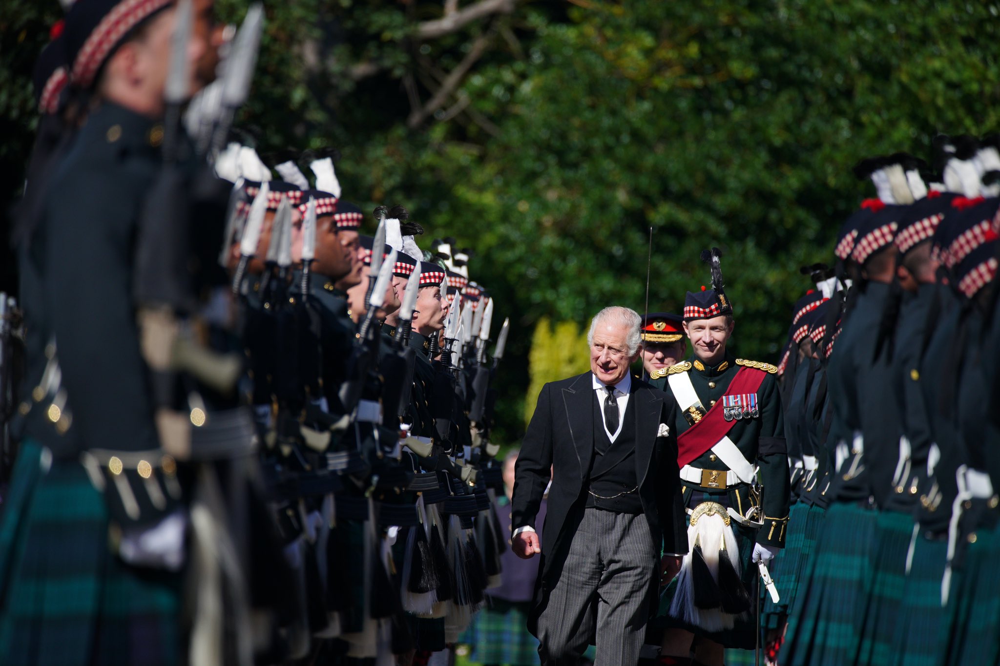 King Charles III in black tailcoat walks in the middle of two rows of military men in kilts in Edinburgh