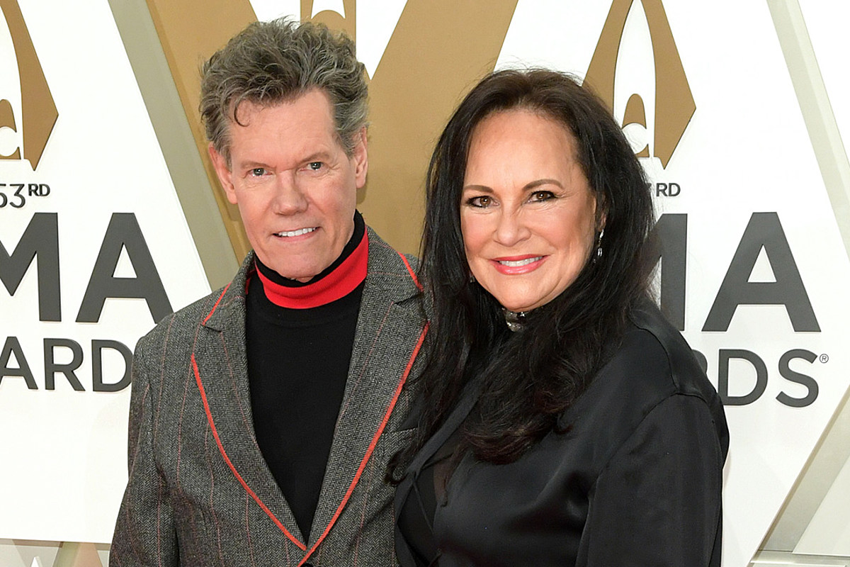 Smiling Randy Travis wearing a red and gray coat and smiling Mary Beougher wearing black top