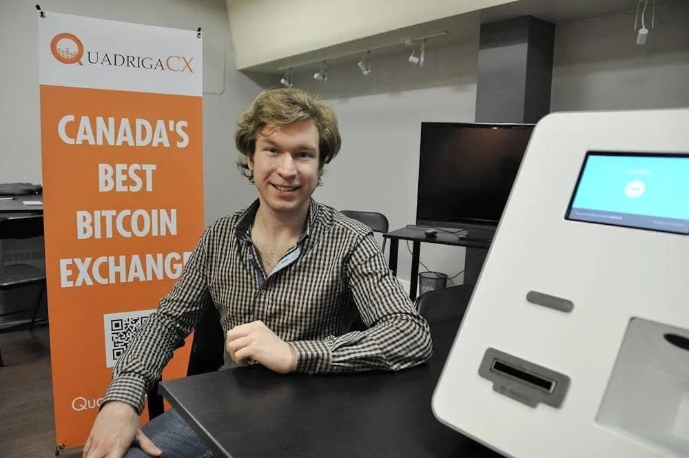 Gerald Cotton in a stripe long sleeve shirt seated beside a Bitcoin ATM machine at the Quadriga office in Canada