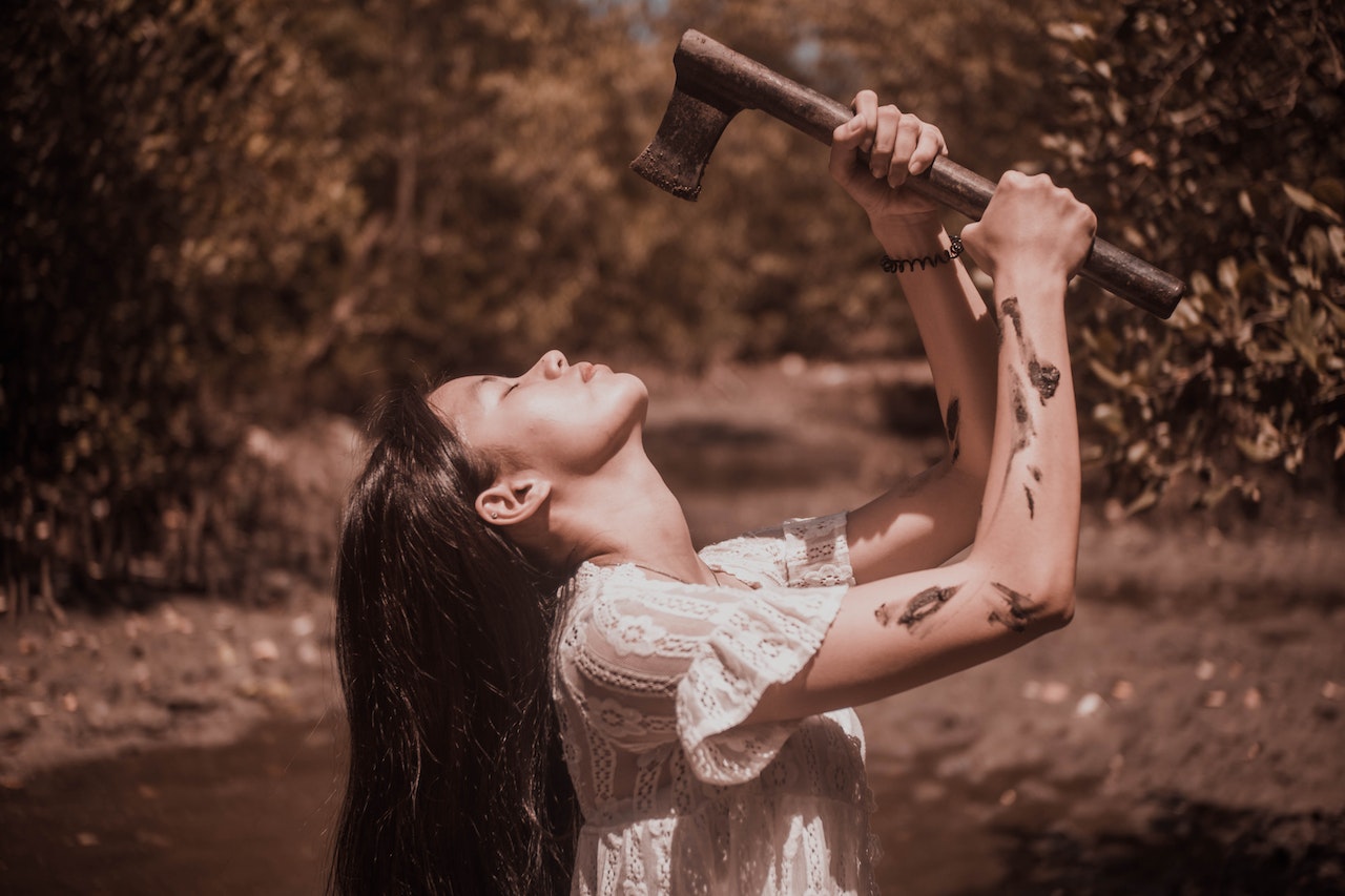 Calm young Asian woman holding axe in hands in woods