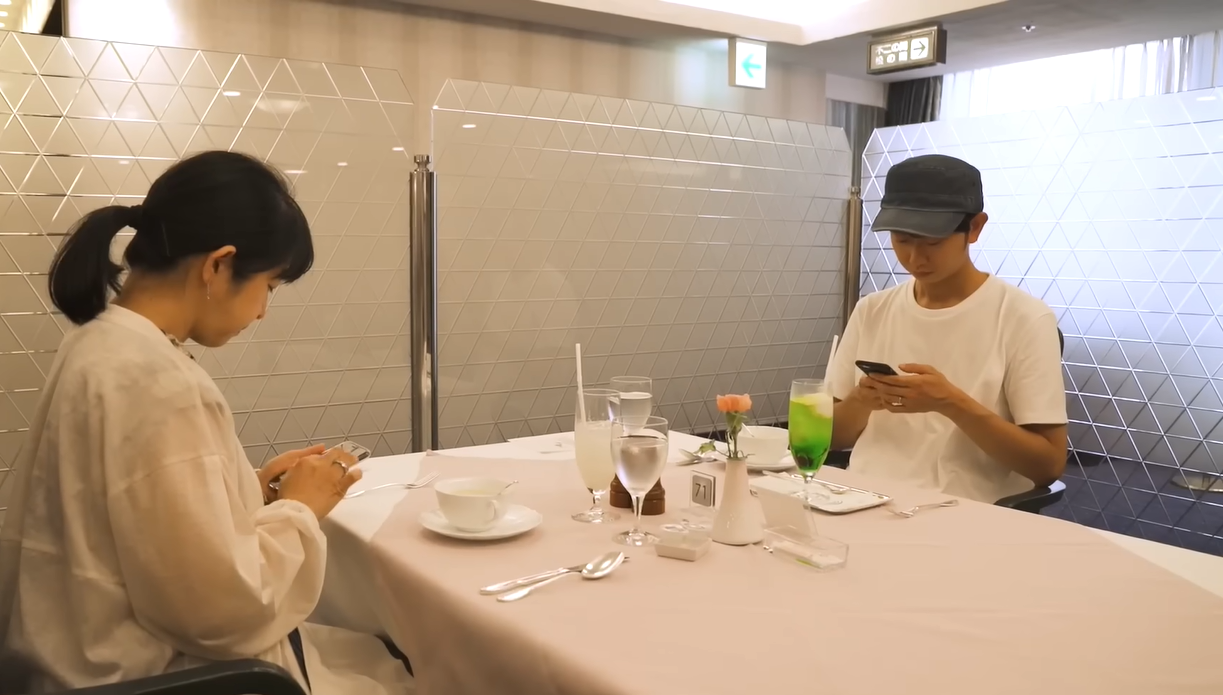 Shoji Morimoto and female client check their phone while seated across each other in restaurant
