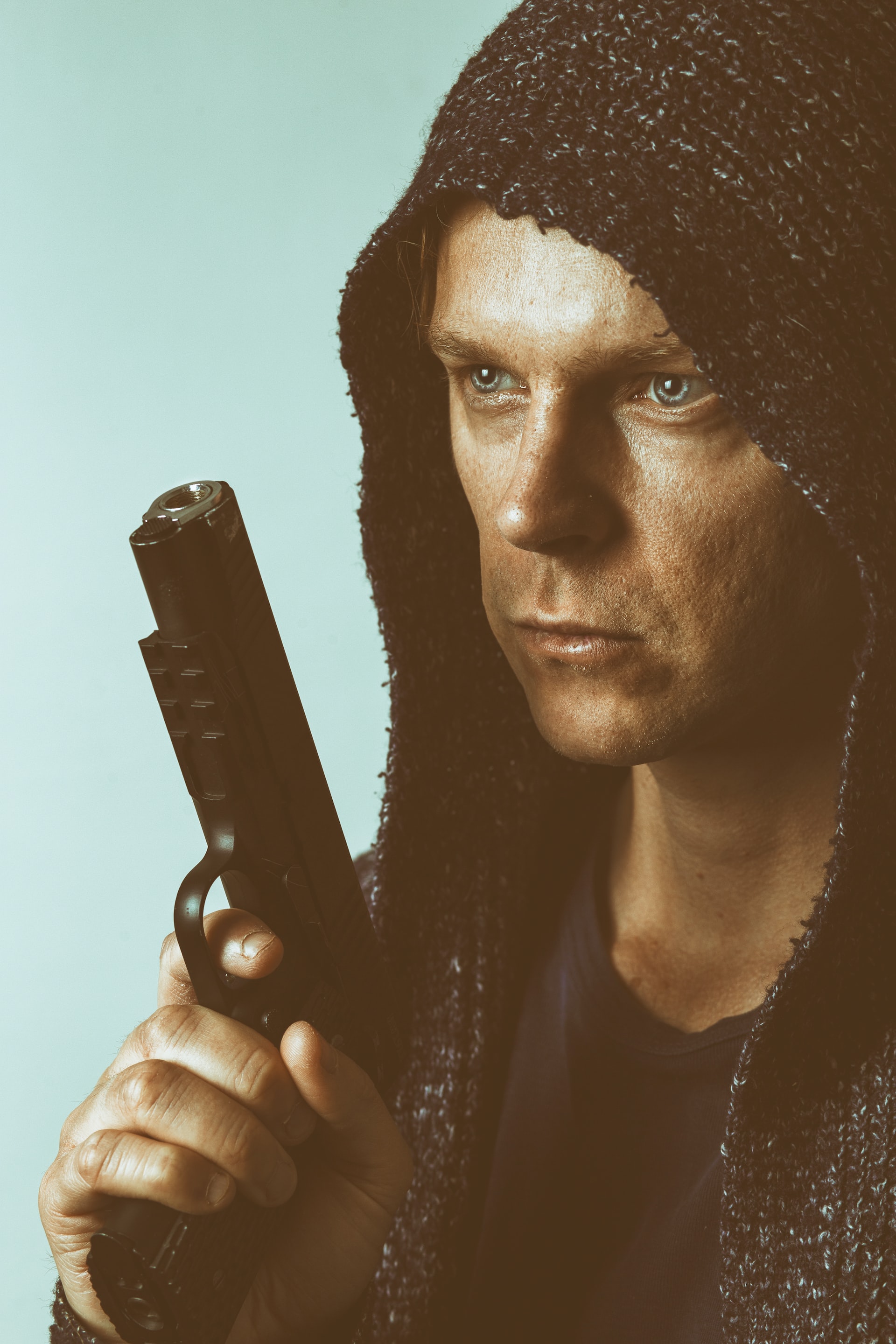 A hooded man is holding a pistol in his hand