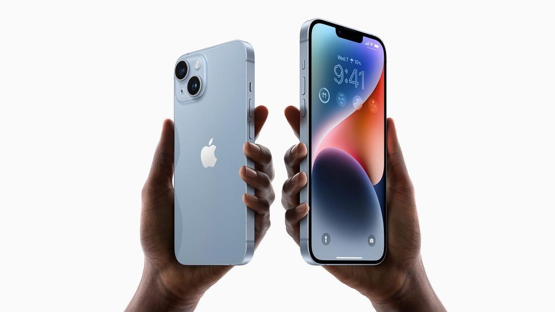 A hand holds a blue iPhone 14 with its back shown and a hand with a blue iPhone 14 Plus with its front shown