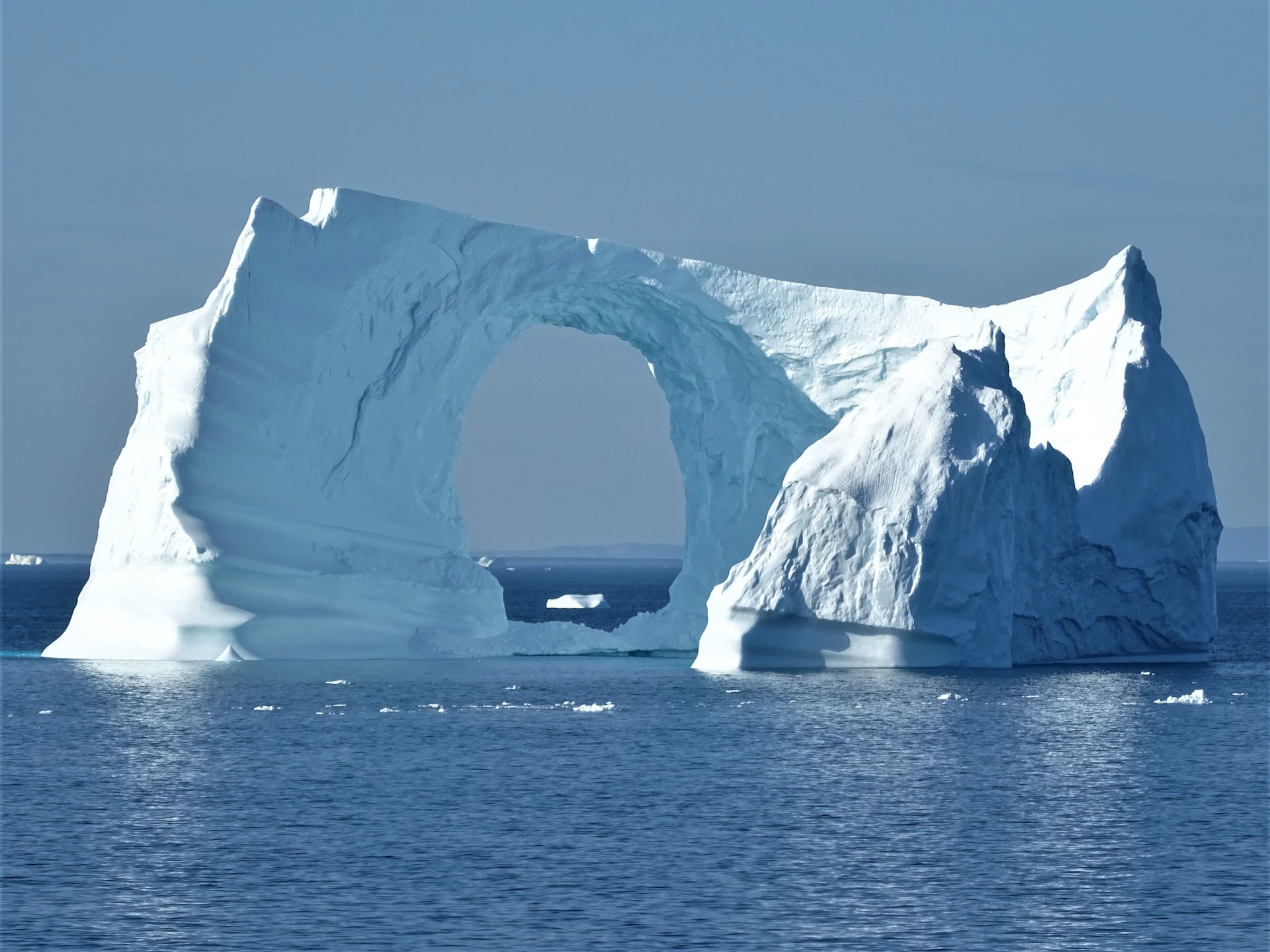 A giant iceberg floating alone on the sea, with an enormous hole near the middle part