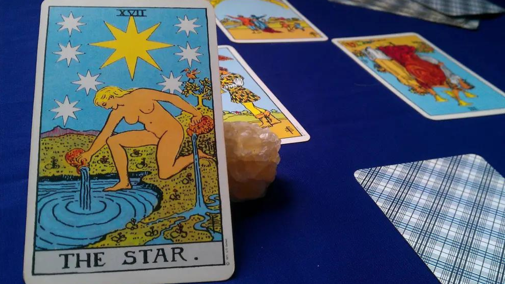 The Star Upright Card placed on a blue table along with other cards and a crystal