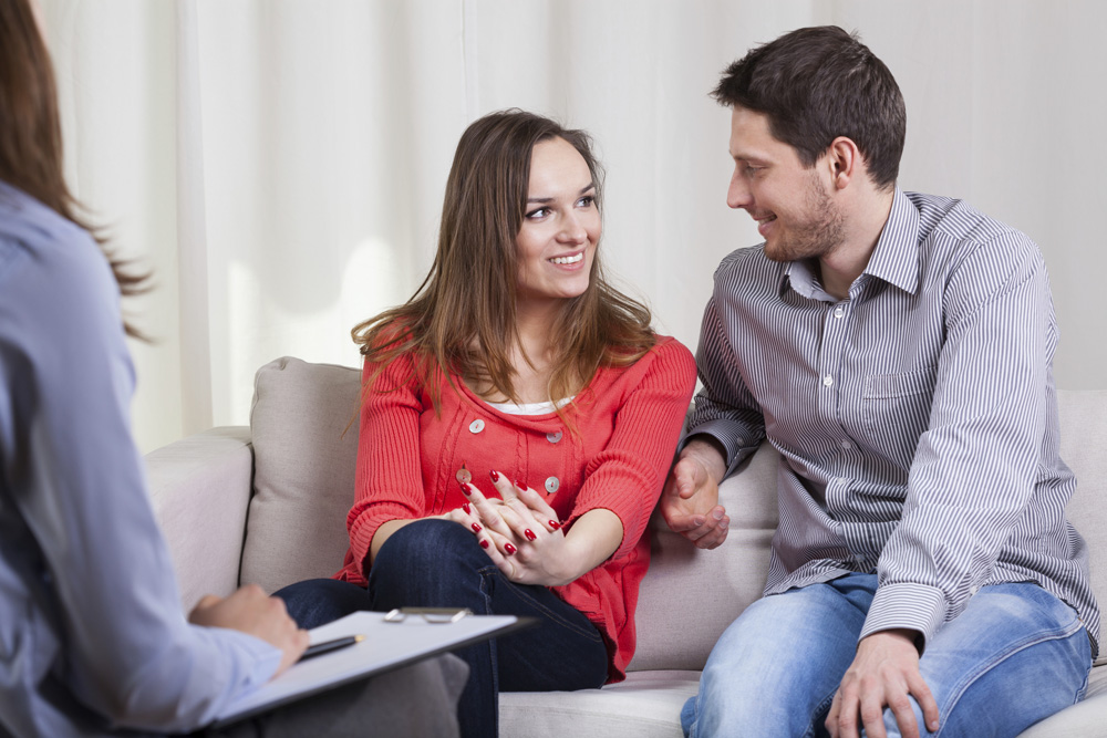 A lady dating consultant talking to a man and woman while sitting on a couch