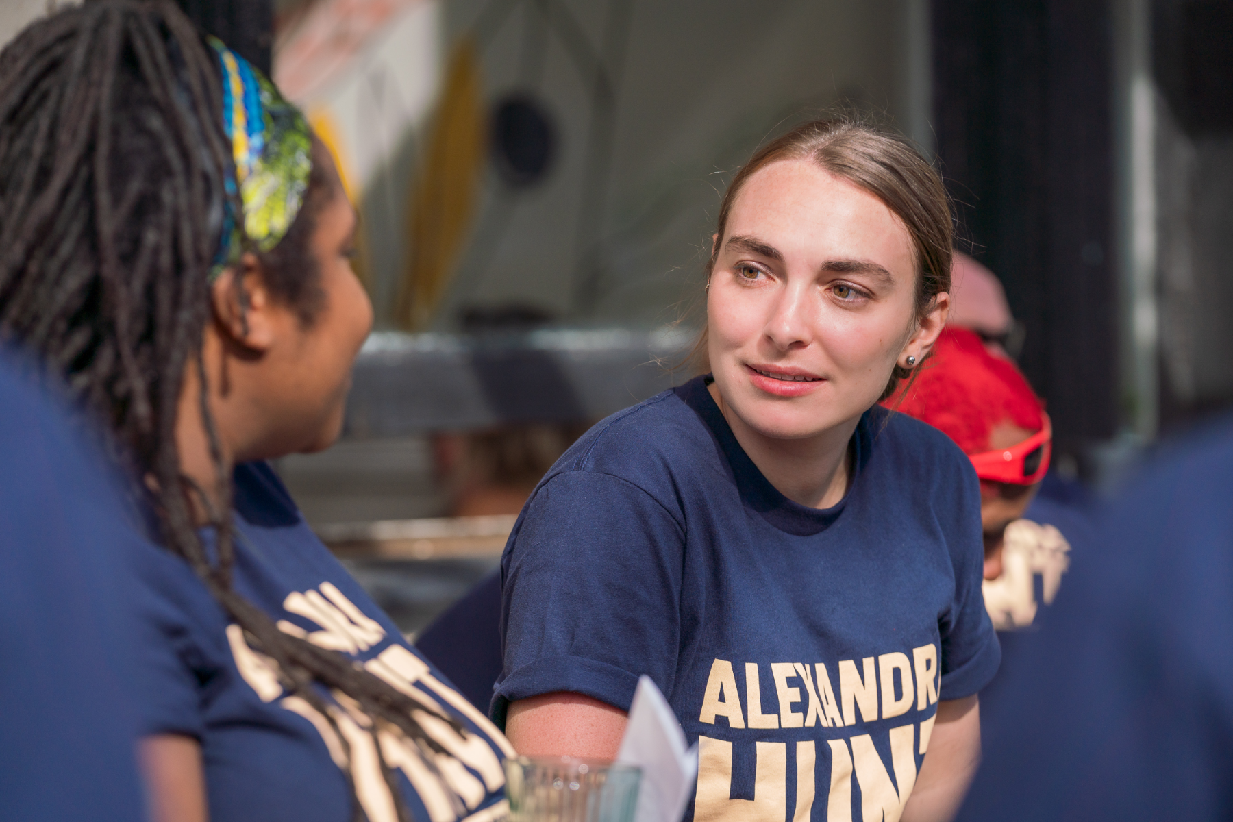Alexandra Hunt talks to a black girl while wearing a blue shirt with her name on it