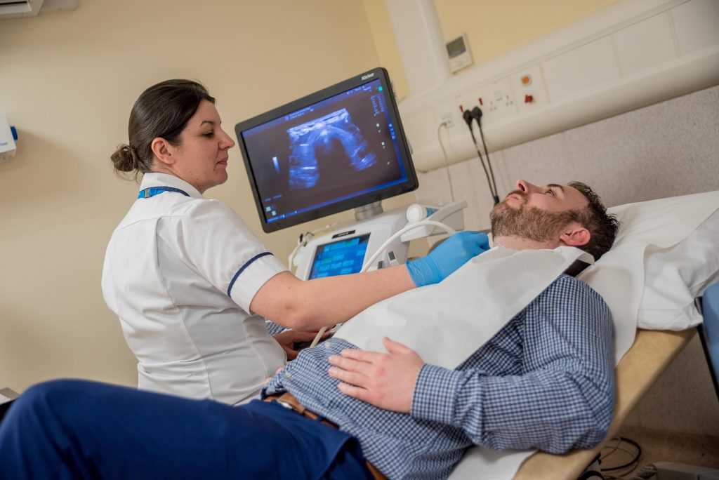 A nurse carrying out an ultrasound on a man's neck while looking at the neck