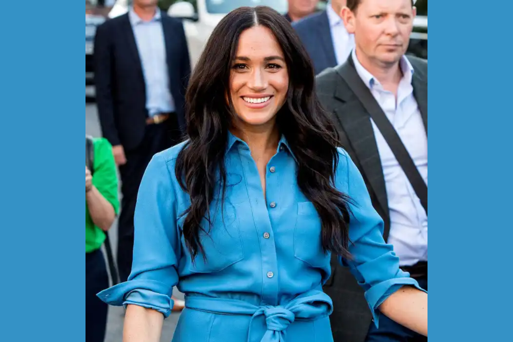 Meghan Markle, dressed in blue, smiles as she walks in public
