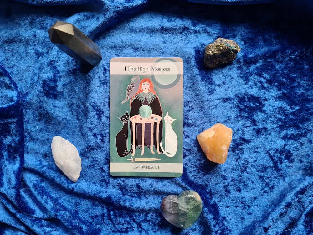 A tarot card placed on top of a blue cloth along with some colorful stones