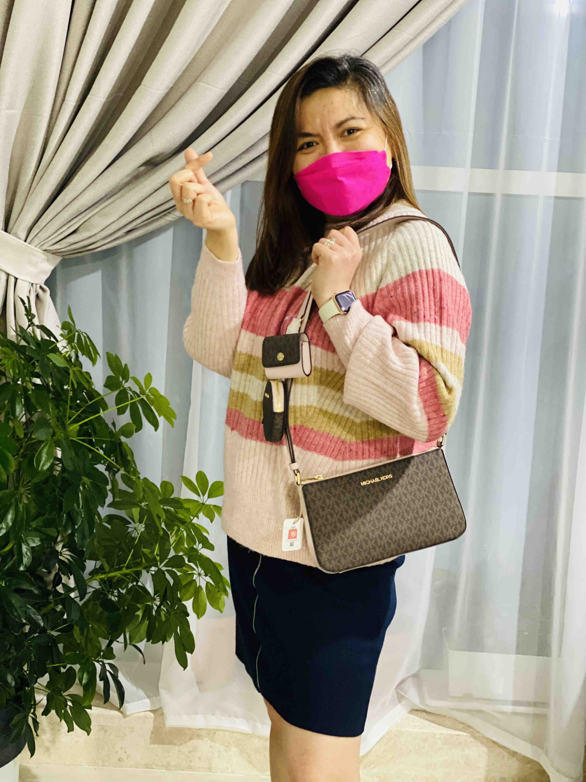 A woman carrying a jet set bag while doing a finger heart