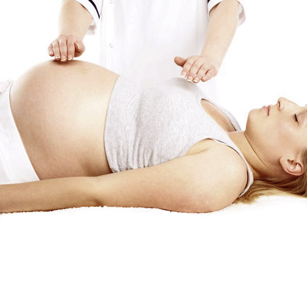 A pregnant woman lying in a massage table while eyes are closed and receiving Reiki session