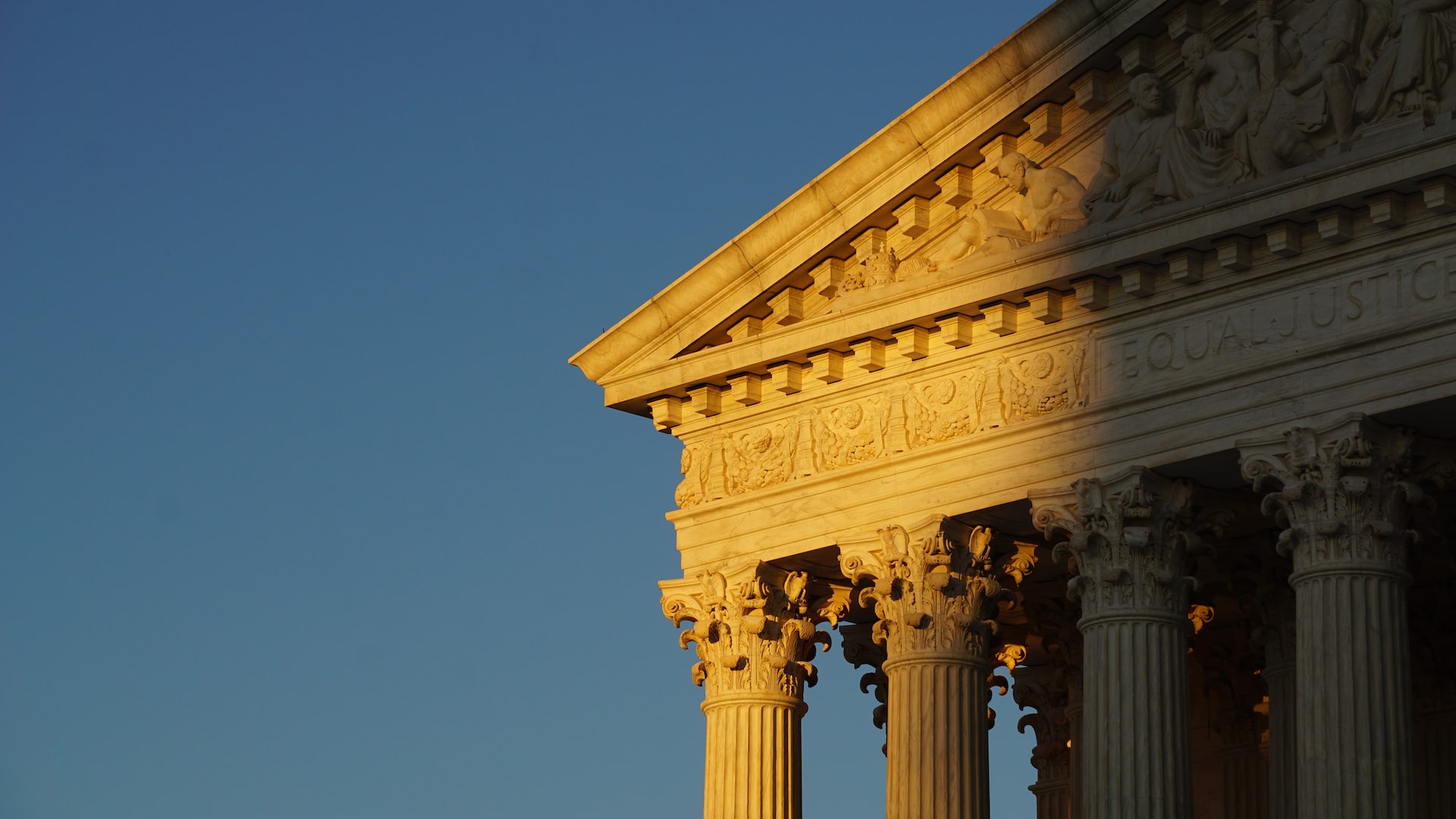 Partly shaded upper left corner of the U.S. Supreme Court and its columns against a cloudless light blue sky