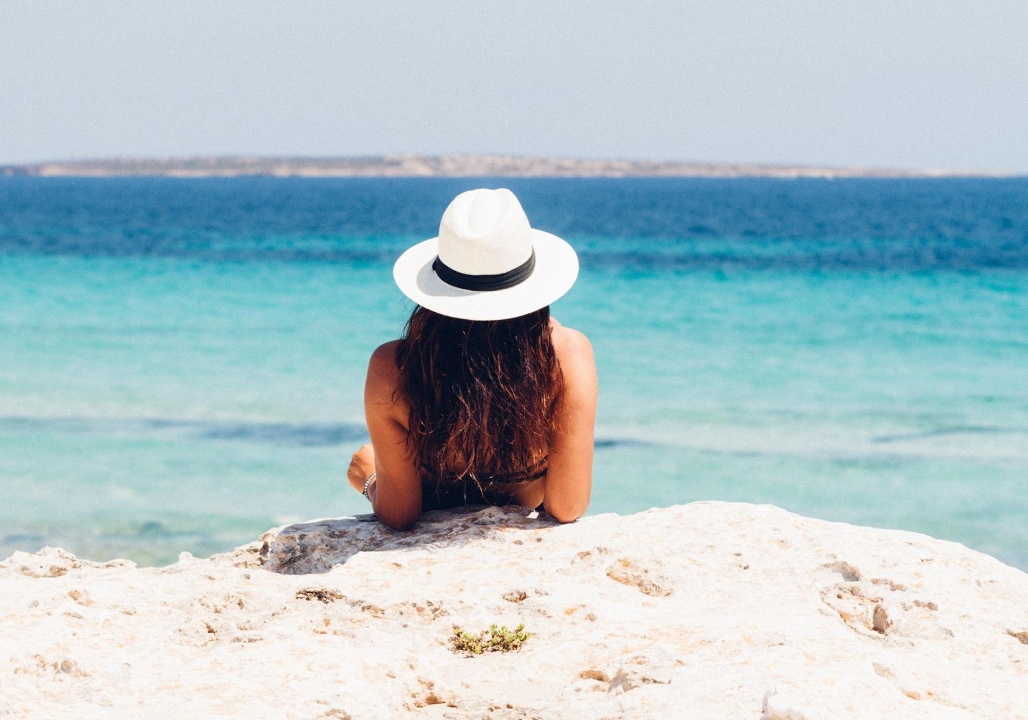 A woman wearing a hat alone at the beach