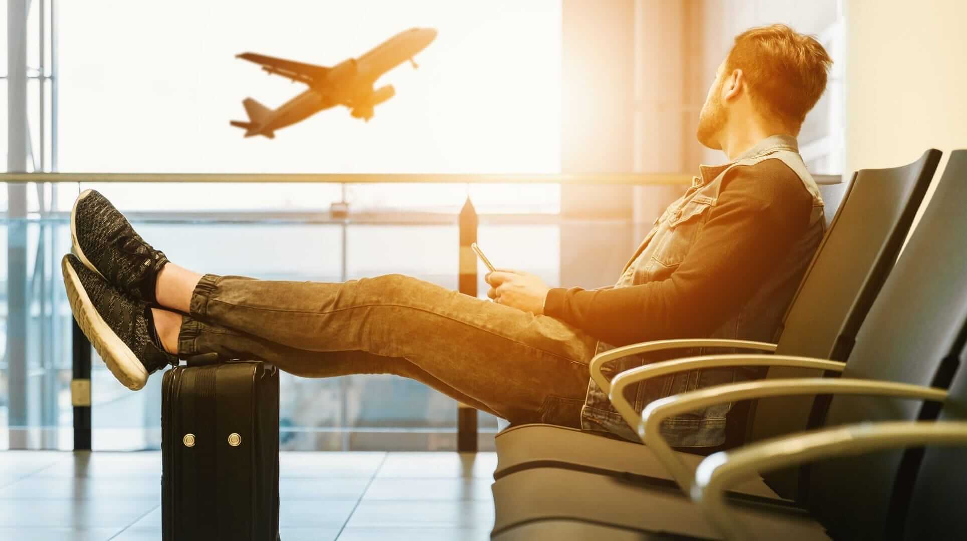 A man sitting at the airport looking at a plane in midair