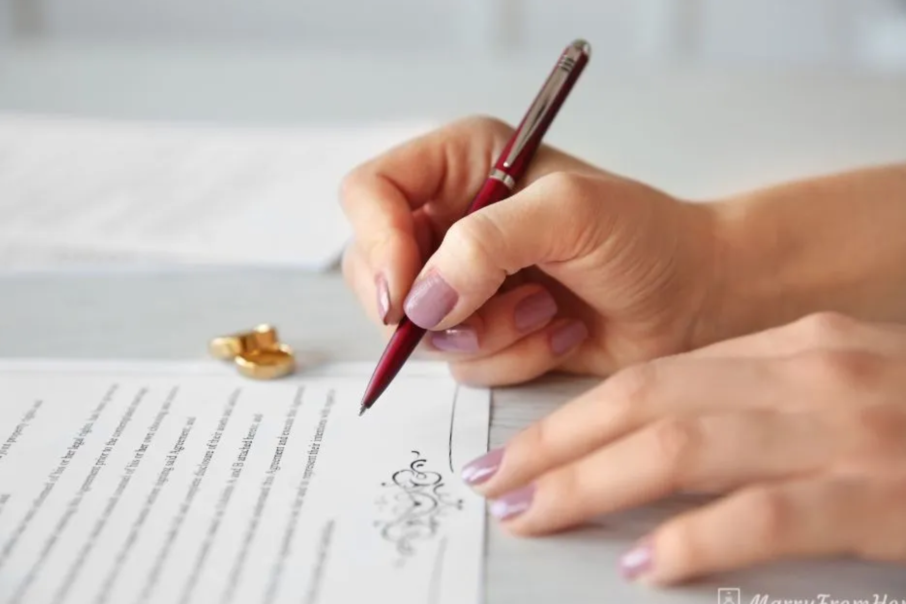 A woman's hand signing a form with a ring next to the paper