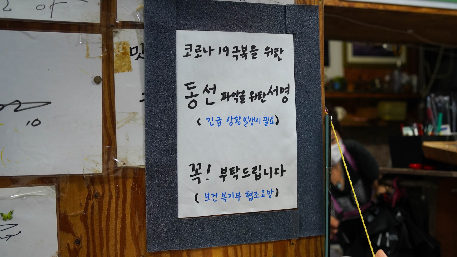 A COVID-19 notice on black and blue ink on a white paper in Hangul posted on a wall