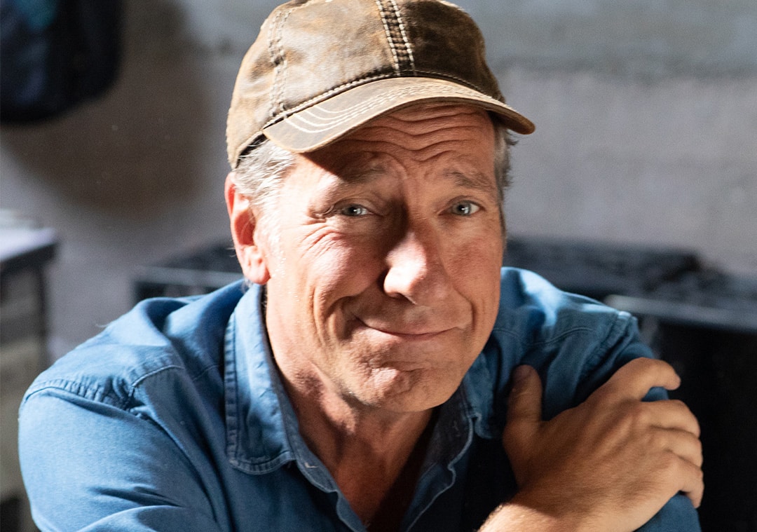 Mike Rowe wearing a blue jean t-shirt and a brown face cap while his hands are folded