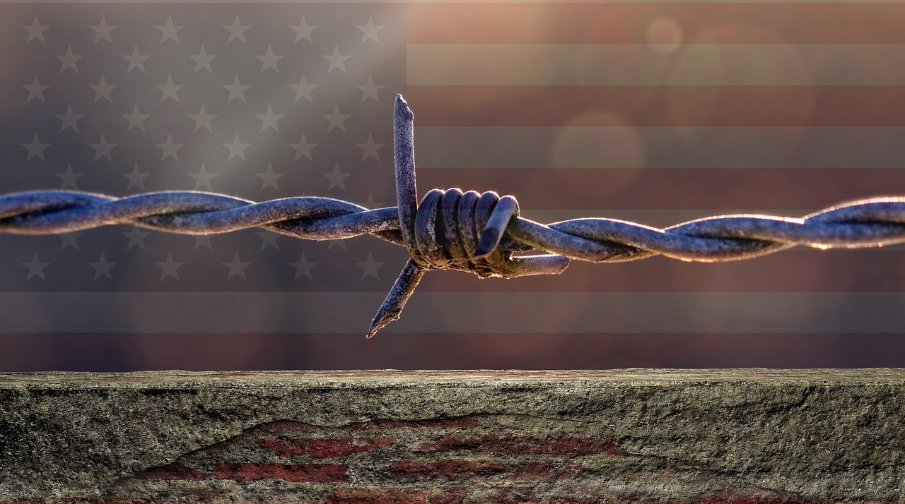 A barbed wire with the U.S. flag blurred in the background