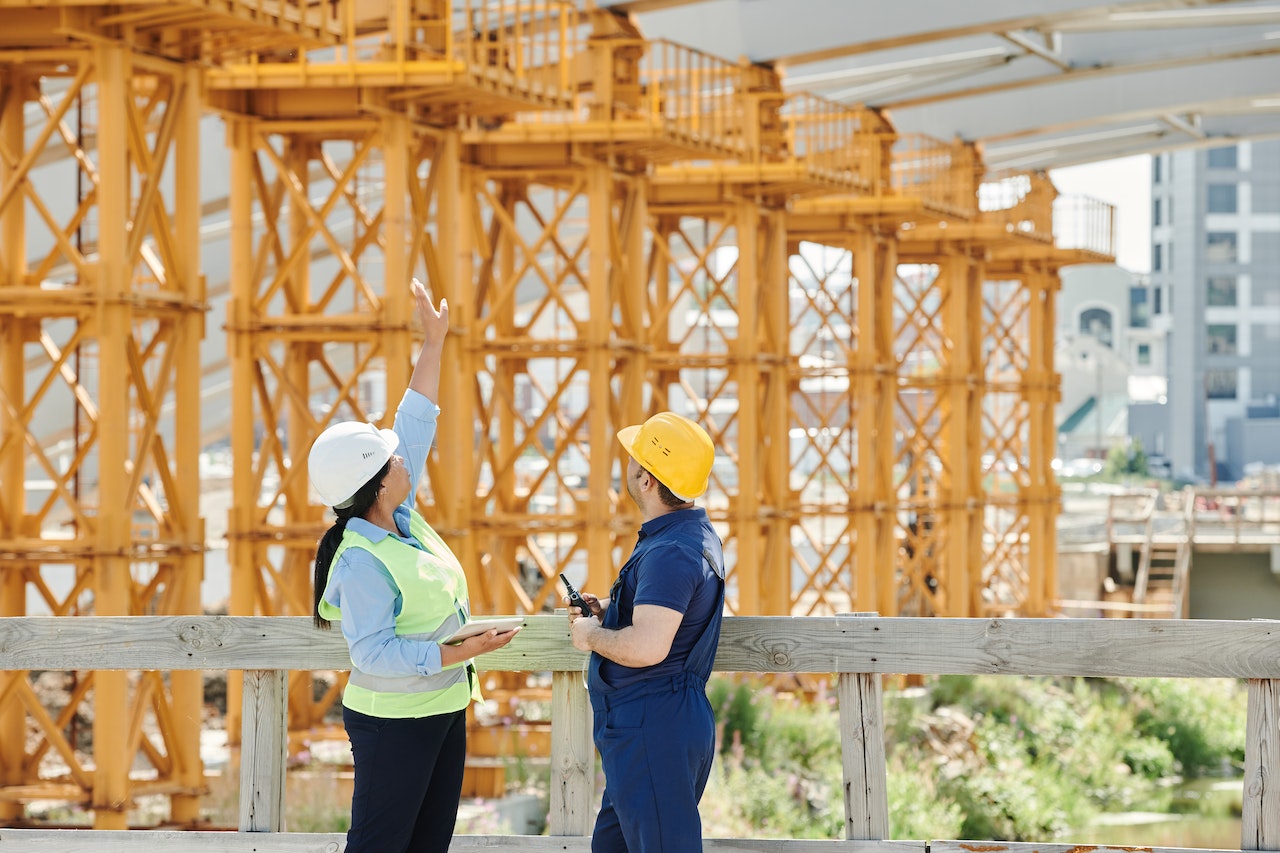 A Man and a Woman with PPEs Talking at a Construction Site