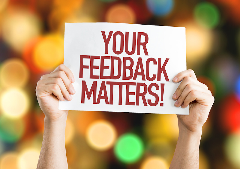 A woman's hand holding a piece of paper with the words "Your Feedback Matters!"
