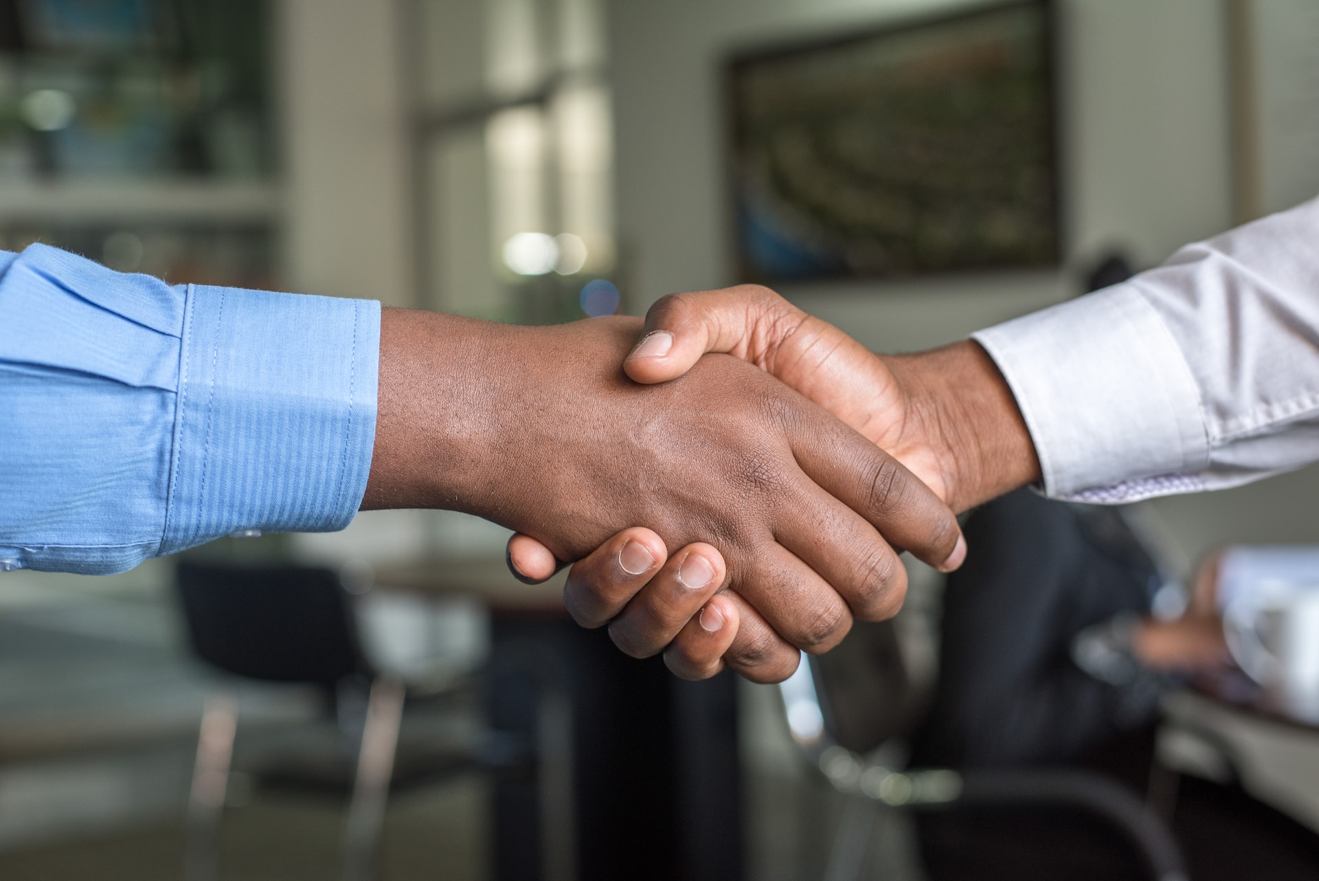 Two African American men in long sleeve shirts shake hands after signing a business partnership