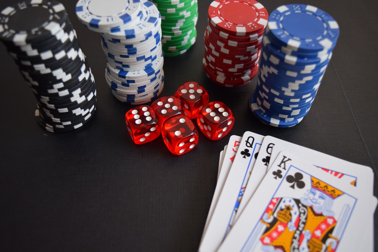 Five red dice, a stack of cards, and five stacks of casino chips beside each other